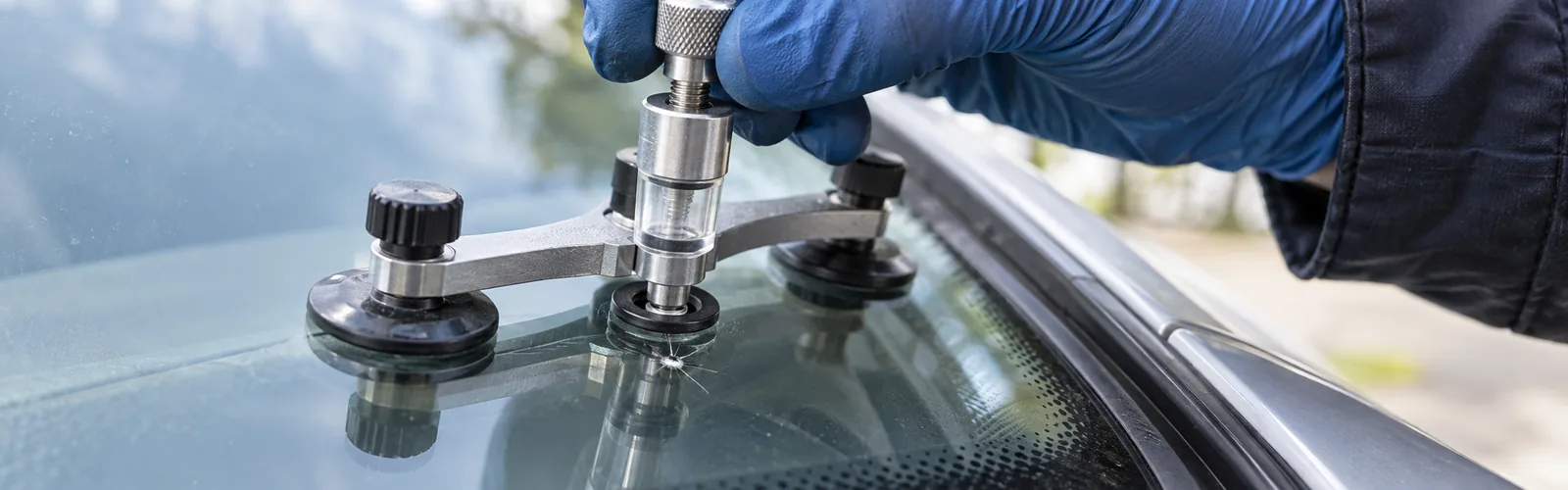 A gloved hand positioning an auto glass tool over a small windshield chip
